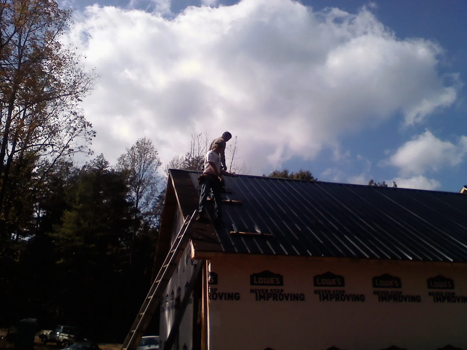 Roofer fastening dark metal panels high against a cloudy sky, from a Roof Inspection job in Andover